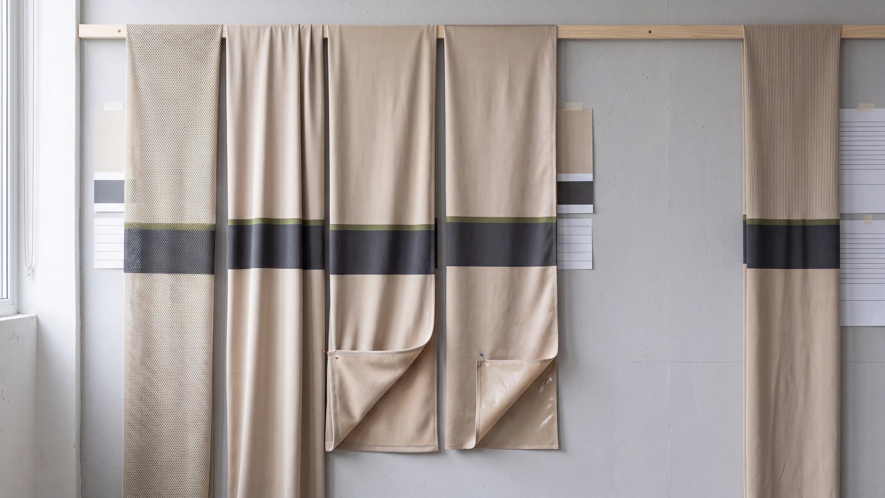 Five base fabrics hanging side by side from one rail, printed with the same design, from open mesh to a laminate with its film backing turned out, and a textured knit hung apart